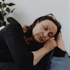 En kvinna vilar på en soffa, ögonen slutna, en bild av djup fatigue svenska.