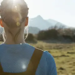 En person står i ett fält med solen i ryggen. Håret är uppsatt och en del hänger ner längs nacken, som ett tecken på inre stress.