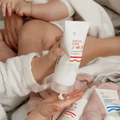 En bebis med torr hud får mjukgörande hudkräm på handen. Två tuber med "Special Care Junior" syns.