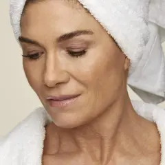 En kvinna med handduk på huvudet och i morgonrock, som visar upp sin hud. Hon kanske använder retinol solskydd för att skydda sig.