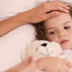 En mamma känner sitt barns panna. Barnet har en nalle och ser lite trött ut, kanske magsjuk. Dags för Ipren eller Alvedon?