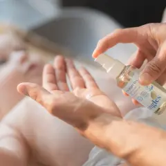 En hand sprutar olja i en annan hand, redo att smörja en bebis med skorv. Mjuk och varsam vård för den lilla huden.