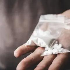En hand håller en plastpåse med vitt pulver och tabletter, potentiellt crystal meth.