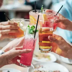 Händer som skålar med färgglada drinkar. En känsla av gemenskap, men för vissa kan alkoholen leda till ångest.