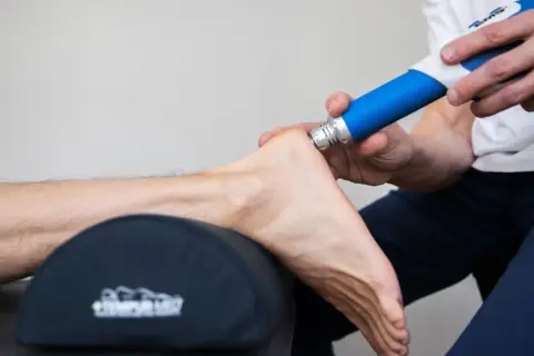Fascia behandling biverkningar: En terapeut använder en blå enhet för att behandla en fot.
