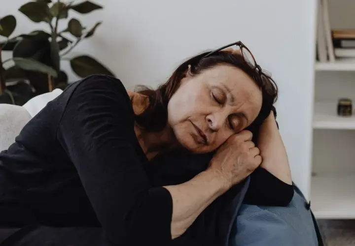 En kvinna vilar på en soffa, ögonen slutna, en bild av djup fatigue svenska.