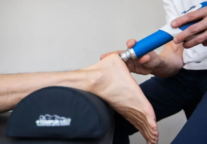 Fascia behandling biverkningar: En terapeut använder en blå enhet för att behandla en fot.
