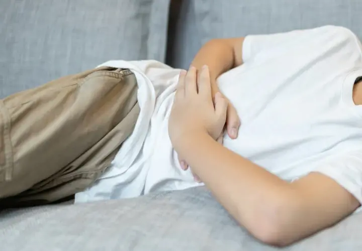 Barnet ligger på en soffa och håller sig om magen, troligen för att det har ont i magen.