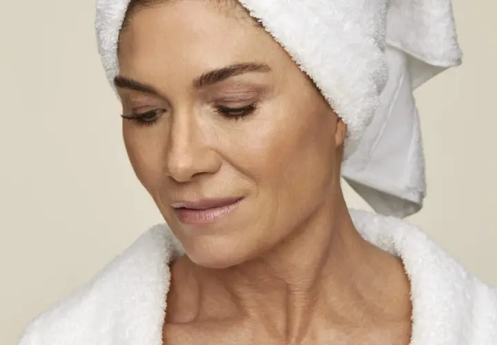 En kvinna med handduk på huvudet och i morgonrock, som visar upp sin hud. Hon kanske använder retinol solskydd för att skydda sig.