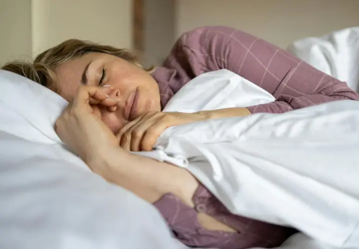 Kvinna sover oroligt, kanske bara sova 5 timmar per natt. Hon ligger i sängen med en näsgrimma.