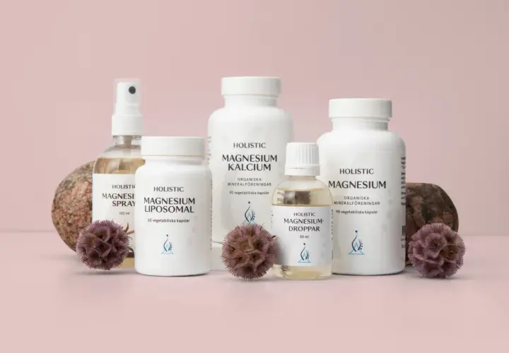 Holistisk medicin: flaskor med magnesiumprodukter, spray, kapslar och droppar, omgivna av stenar och torkade blommor.