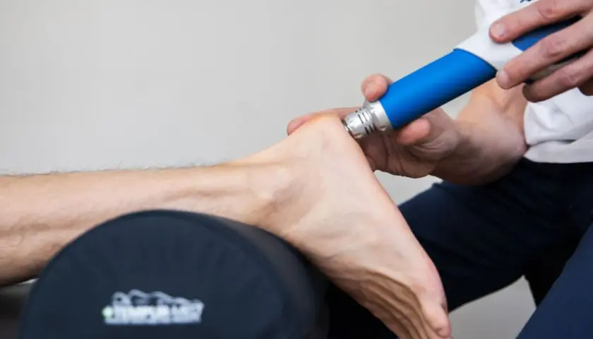 Fascia behandling biverkningar: En terapeut använder en blå enhet för att behandla en fot.