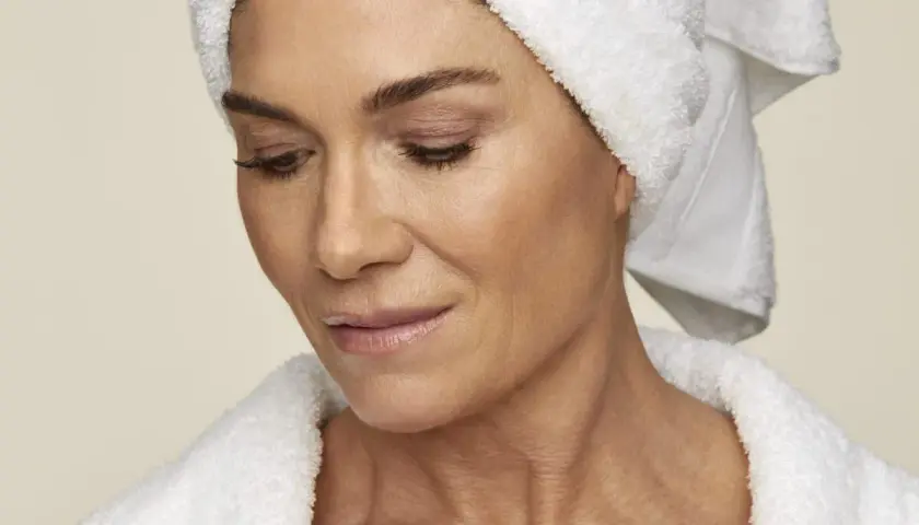 En kvinna med handduk på huvudet och i morgonrock, som visar upp sin hud. Hon kanske använder retinol solskydd för att skydda sig.