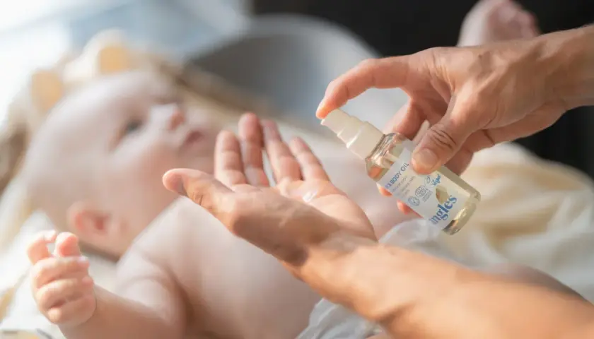 En hand sprutar olja i en annan hand, redo att smörja en bebis med skorv. Mjuk och varsam vård för den lilla huden.