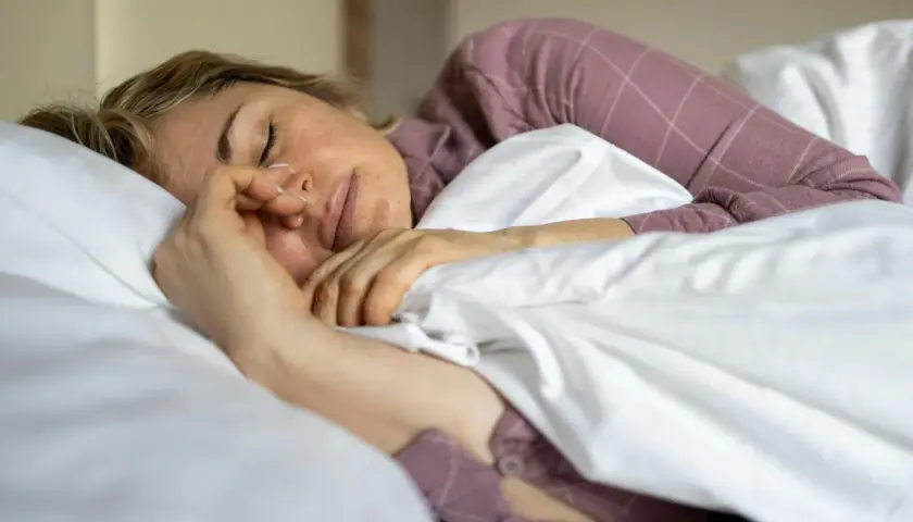 Kvinna sover oroligt, kanske bara sova 5 timmar per natt. Hon ligger i sängen med en näsgrimma.