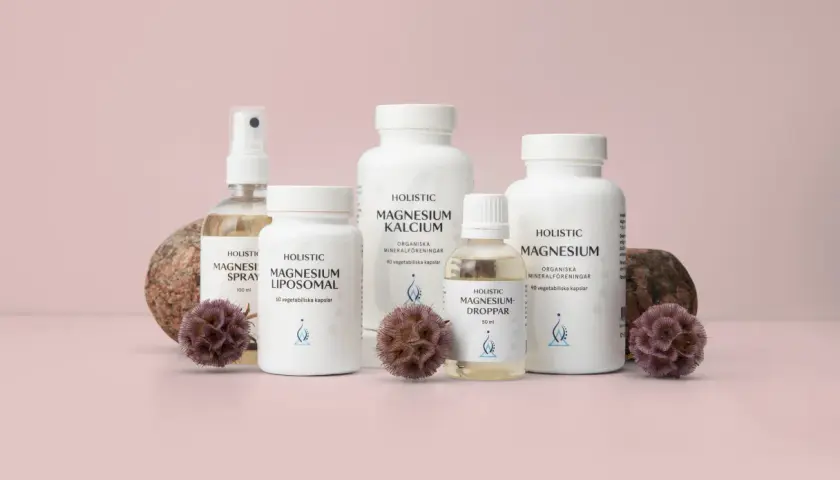 Holistisk medicin: flaskor med magnesiumprodukter, spray, kapslar och droppar, omgivna av stenar och torkade blommor.