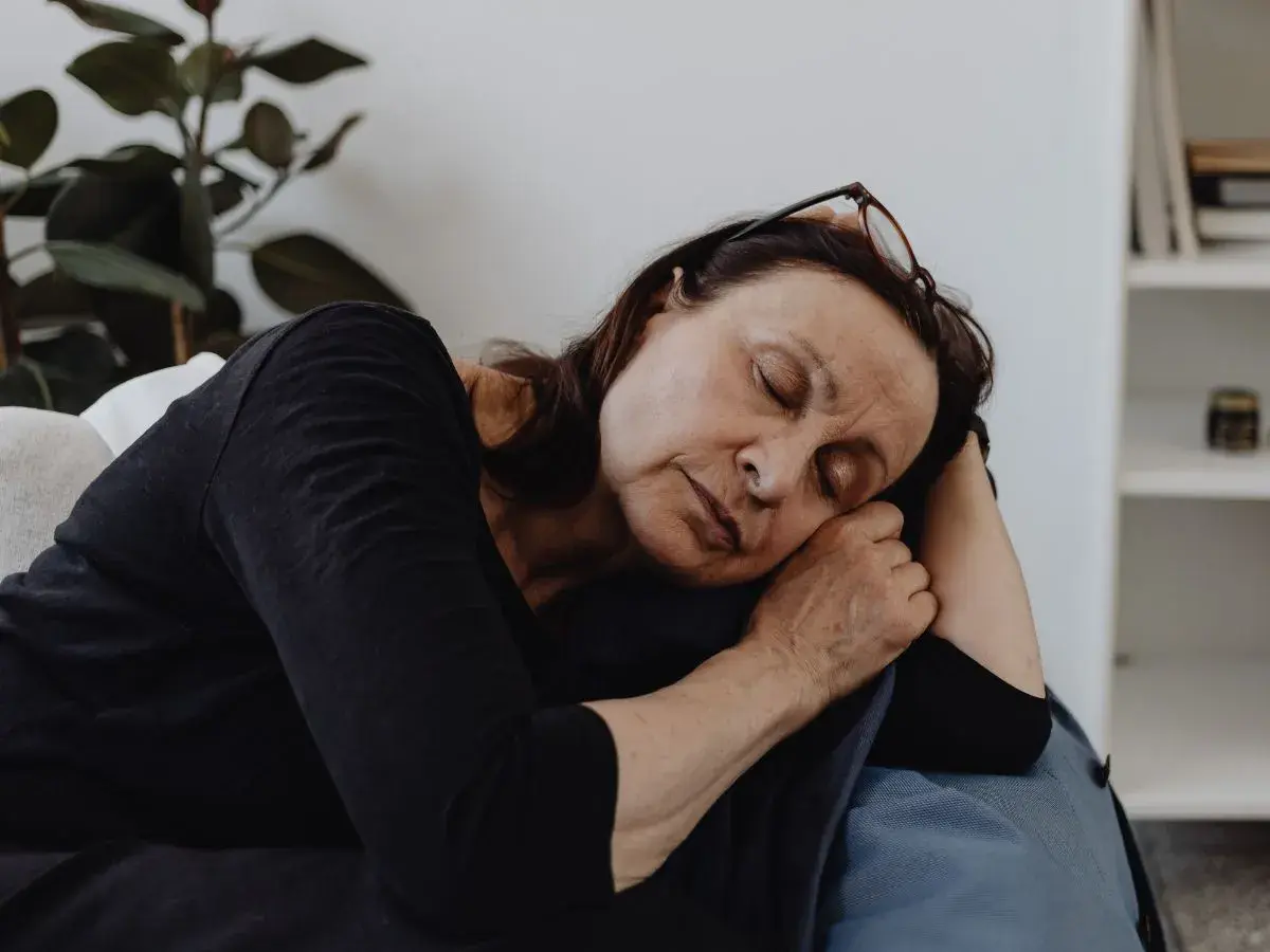 En kvinna vilar på en soffa, ögonen slutna, en bild av djup fatigue svenska.