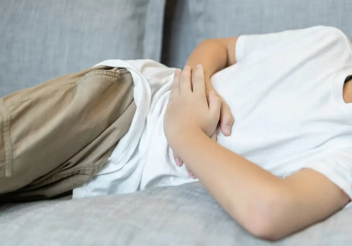 Barnet ligger på en soffa och håller sig om magen, troligen för att det har ont i magen.