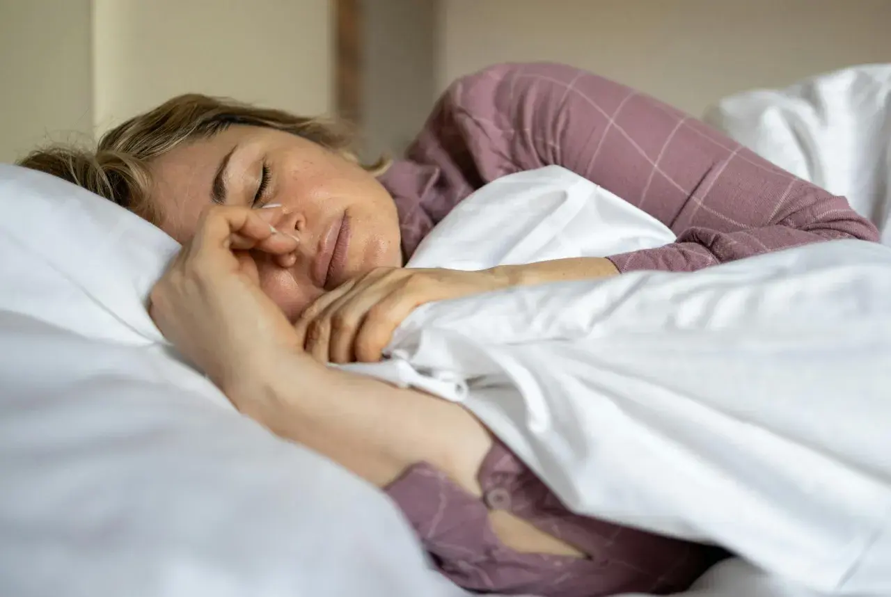 Kvinna sover oroligt, kanske bara sova 5 timmar per natt. Hon ligger i sängen med en näsgrimma.