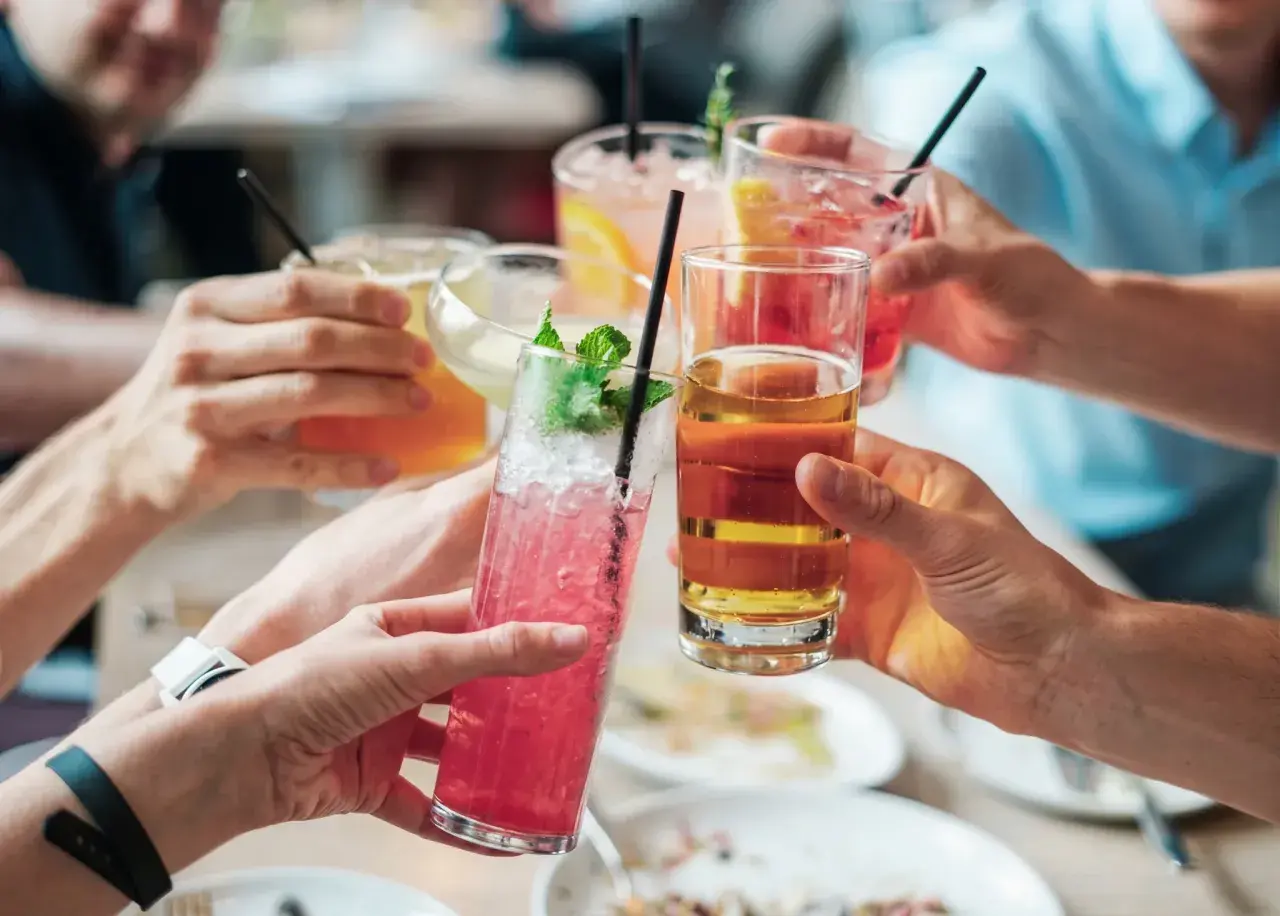 Händer som skålar med färgglada drinkar. En känsla av gemenskap, men för vissa kan alkoholen leda till ångest.