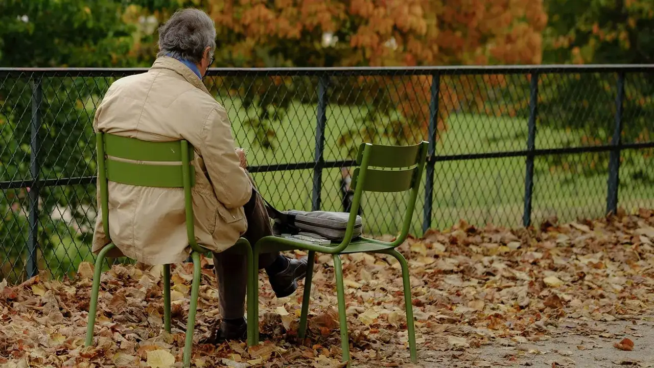 En man sitter ensam p&aring; en parkb&auml;nk i h&ouml;stl&ouml;ven, en bild av ensamhet i Sverige.