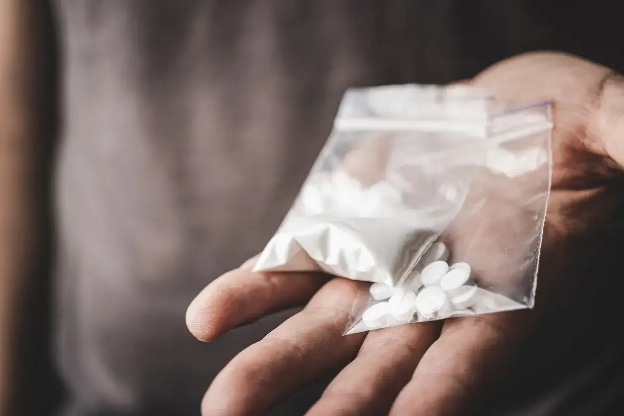 En hand håller en plastpåse med vitt pulver och tabletter, potentiellt crystal meth.